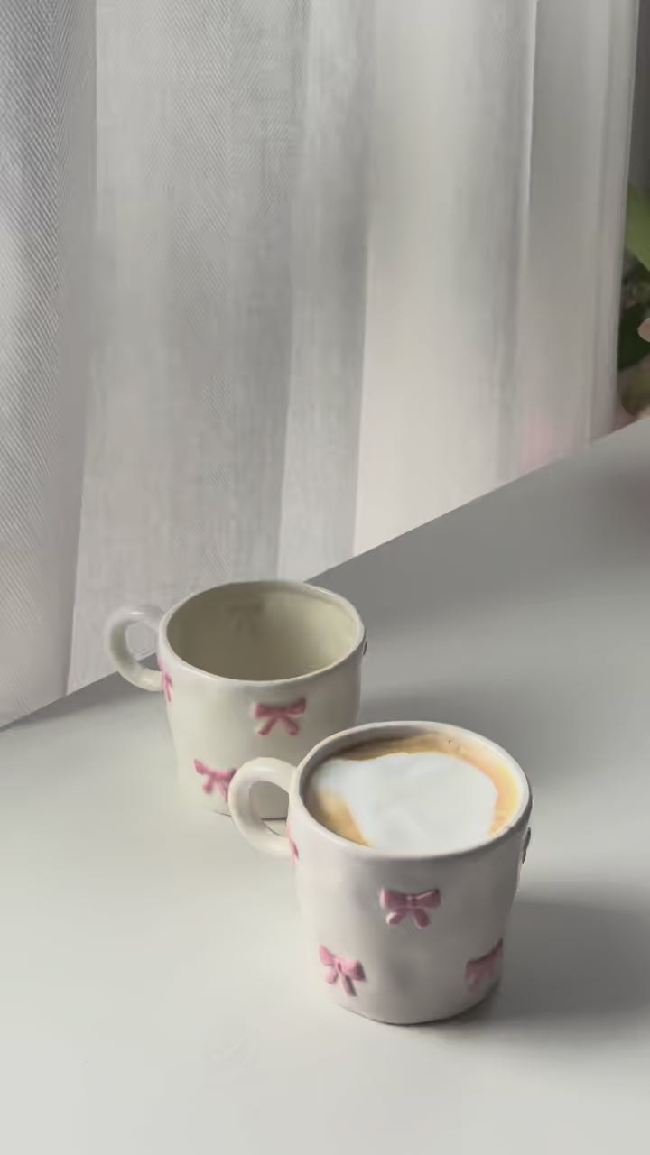 Two pink bow mugs on a white table by the window