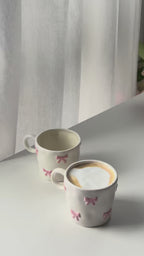 Two pink bow mugs on a white table by the window