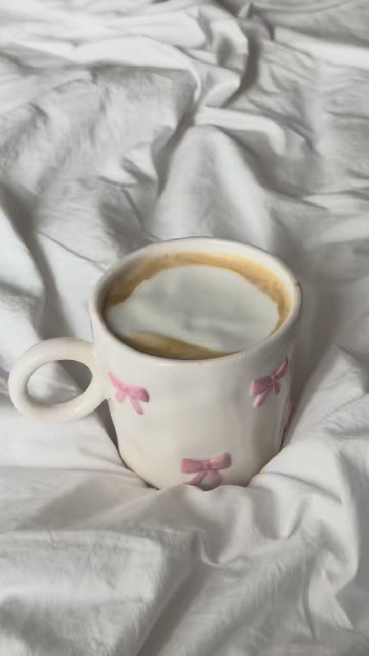 Pink bow mug with latte on white bedding